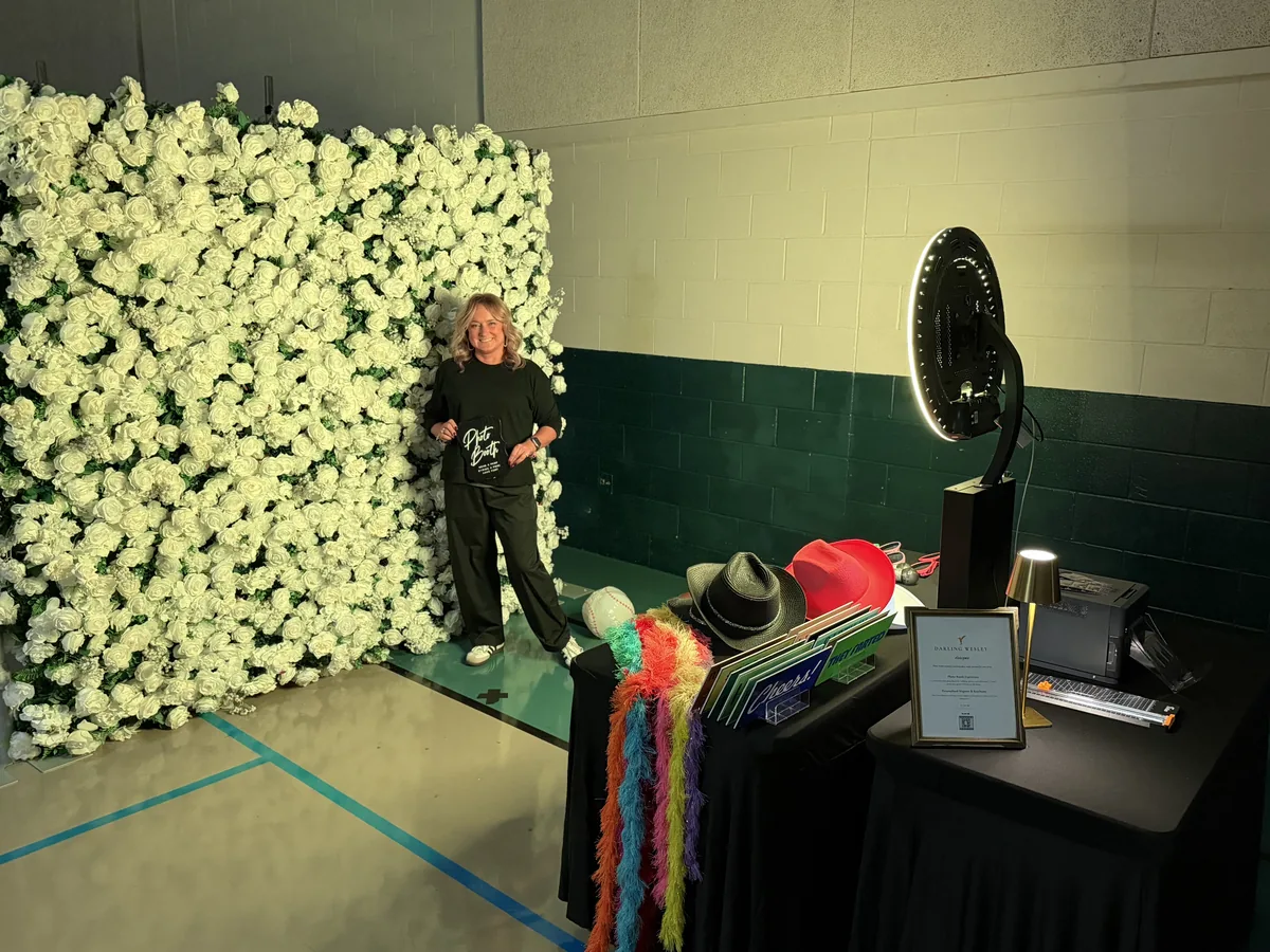 Photo booth station with colorful handheld props beside a white floral backdrop